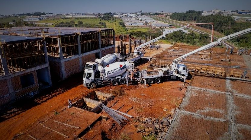 Vista aérea de concretagem de laje em obra comercial, com caminhões-betoneira e bomba lança em operação simultânea